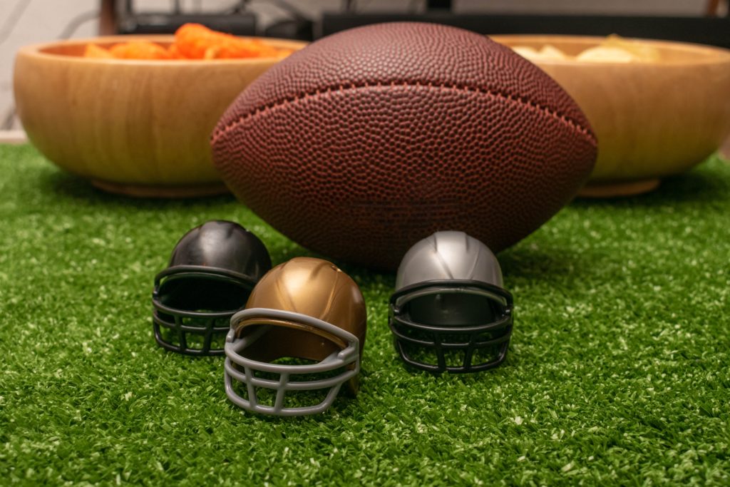 Two bowls of snacks, a football and three tiny helmets on a table.